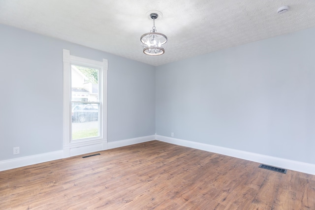 empty room featuring wood finished floors, visible vents, a notable chandelier, and baseboards