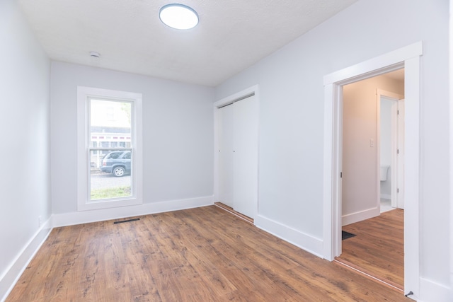 unfurnished bedroom featuring wood finished floors, visible vents, baseboards, and a closet