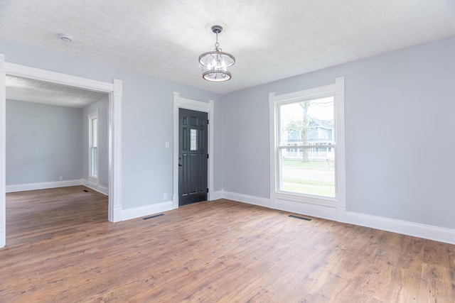 unfurnished room featuring visible vents, wood finished floors, a notable chandelier, and baseboards