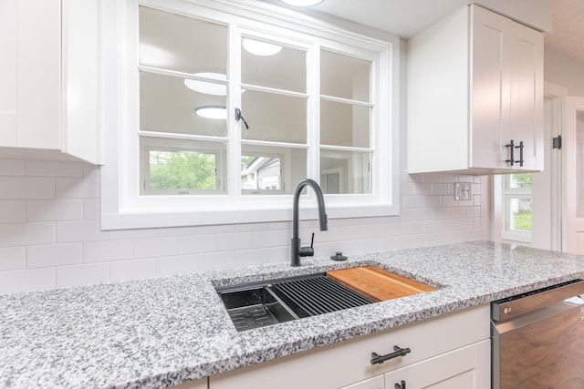 kitchen with tasteful backsplash, dishwasher, white cabinets, and a sink