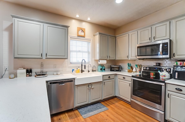 kitchen with gray cabinets, light wood-type flooring, stainless steel appliances, and backsplash