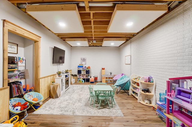 recreation room with brick wall and light hardwood / wood-style floors