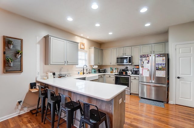 kitchen featuring appliances with stainless steel finishes, sink, light hardwood / wood-style floors, kitchen peninsula, and gray cabinets