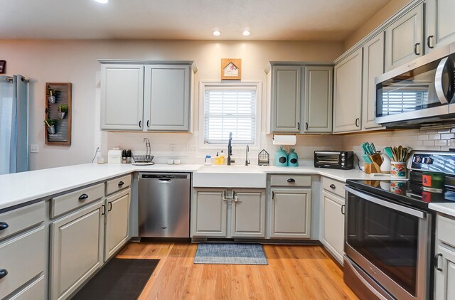 kitchen with light hardwood / wood-style flooring, sink, stainless steel appliances, kitchen peninsula, and gray cabinets