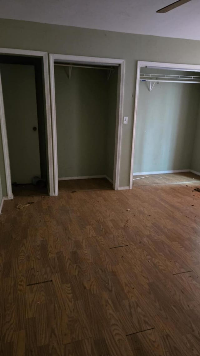 unfurnished bedroom with hardwood / wood-style floors, ceiling fan, and multiple closets