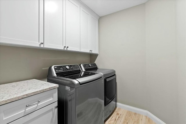 laundry room featuring light wood finished floors, separate washer and dryer, cabinet space, and baseboards