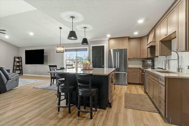 kitchen with light wood finished floors, light stone counters, open floor plan, freestanding refrigerator, and a sink