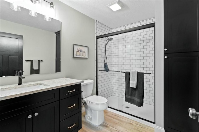 full bathroom featuring a textured ceiling, toilet, wood finished floors, vanity, and a shower stall