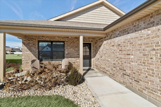 property entrance featuring a shingled roof, covered porch, and brick siding