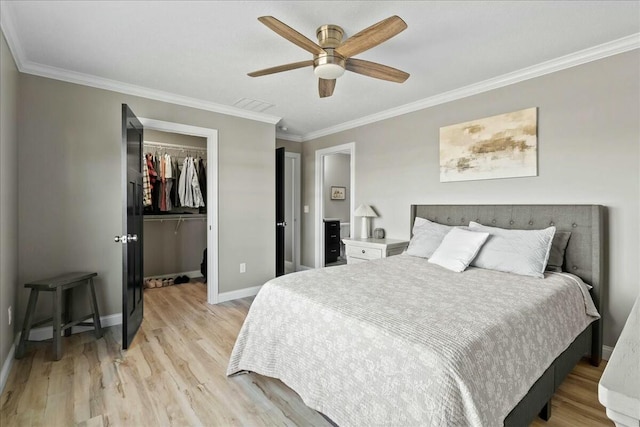 bedroom with baseboards, ornamental molding, a spacious closet, light wood-type flooring, and a closet