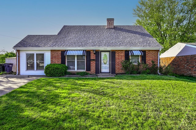 view of front of house with a shingled roof, a chimney, brick siding, and a front yard
