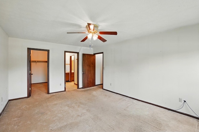1985 Fox Run, Troy, OH 45373 - unfurnished bedroom featuring a walk in closet, light carpet, a closet, ensuite bath, and a ceiling fan