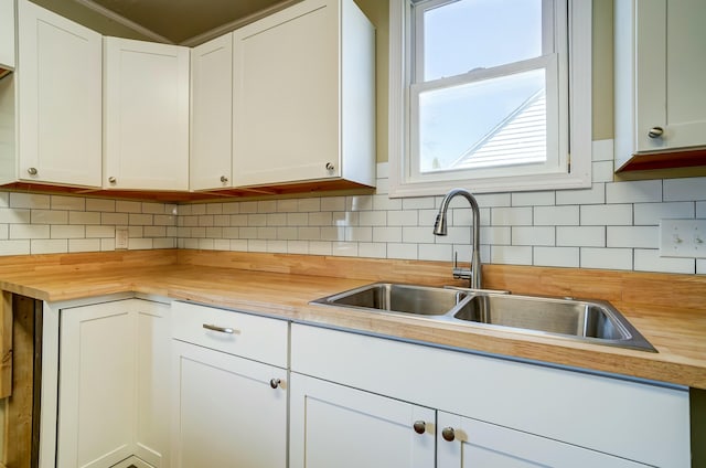 kitchen featuring a sink, wooden counters, backsplash, and white cabinets