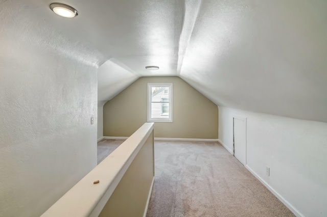 bonus room with a textured ceiling, lofted ceiling, baseboards, and light carpet