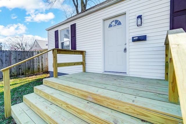 view of exterior entry with a wooden deck and fence