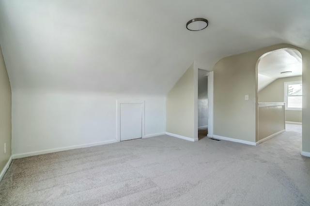 additional living space featuring visible vents, lofted ceiling, arched walkways, carpet floors, and baseboards