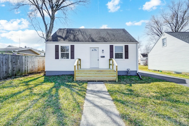 view of front facade with a front yard, fence, and roof with shingles