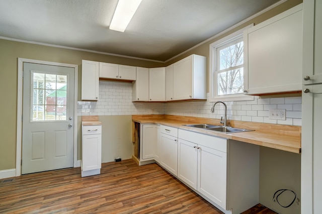 kitchen with wooden counters, decorative backsplash, wood finished floors, white cabinetry, and a sink