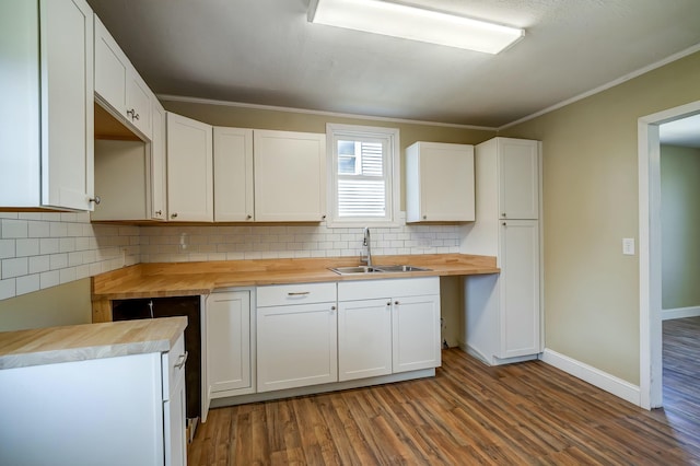 kitchen featuring wood finished floors, wooden counters, ornamental molding, decorative backsplash, and a sink