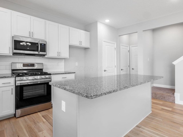 kitchen with stainless steel appliances, a kitchen island, white cabinetry, light wood-style floors, and decorative backsplash