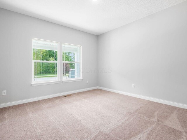 carpeted spare room with a textured ceiling, visible vents, and baseboards