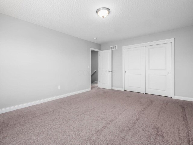 unfurnished bedroom with carpet floors, a textured ceiling, visible vents, and a closet