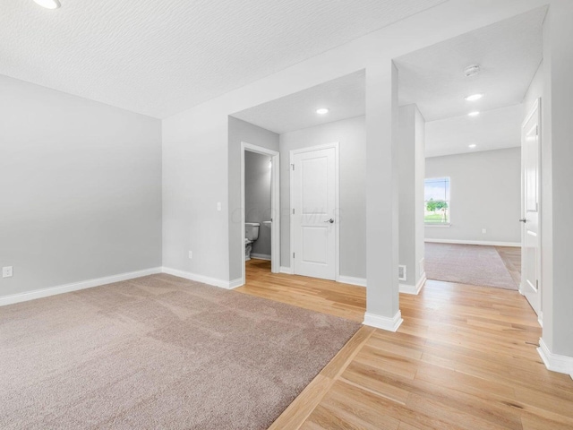 empty room featuring a textured ceiling, recessed lighting, wood finished floors, and baseboards