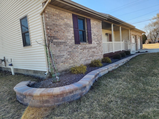 view of side of home with brick siding, covered porch, an attached garage, and a lawn