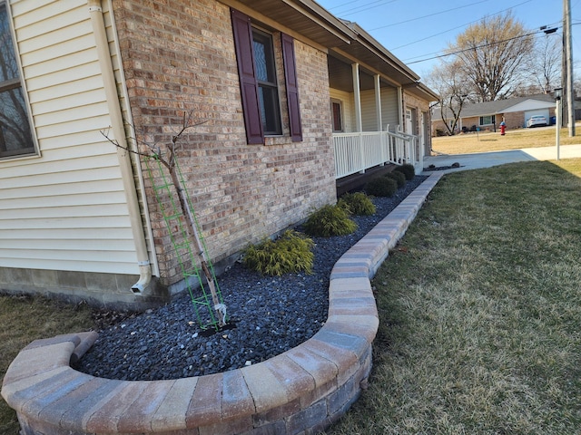 view of side of property featuring a yard, brick siding, and covered porch