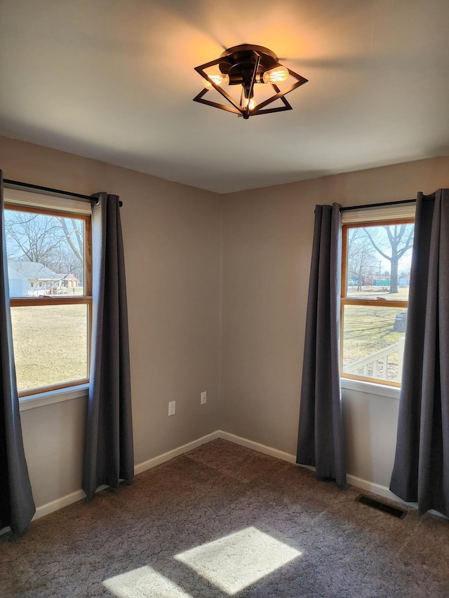 carpeted spare room with a wealth of natural light, visible vents, and baseboards