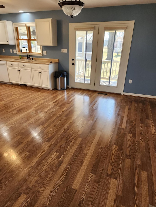 kitchen featuring dark wood-style floors, baseboards, white dishwasher, a sink, and white cabinetry