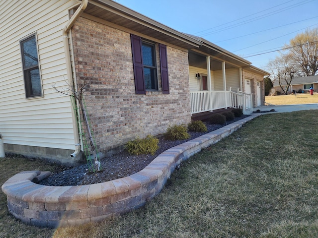 view of side of home featuring a yard, brick siding, a porch, and an attached garage