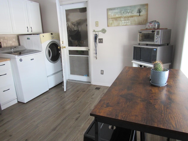 clothes washing area with cabinets, dark wood-type flooring, and washing machine and clothes dryer