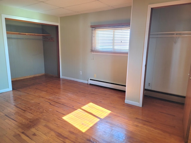 unfurnished bedroom with a paneled ceiling, hardwood / wood-style floors, and baseboard heating