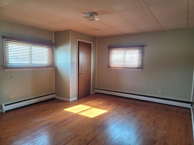 unfurnished bedroom featuring baseboard heating, wood-type flooring, and multiple windows