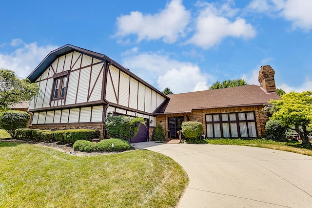 tudor house with a chimney, concrete driveway, a front yard, and brick siding