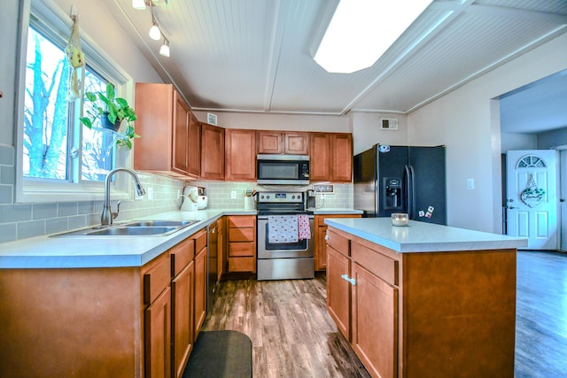 kitchen with sink, a kitchen island, wood-type flooring, and appliances with stainless steel finishes