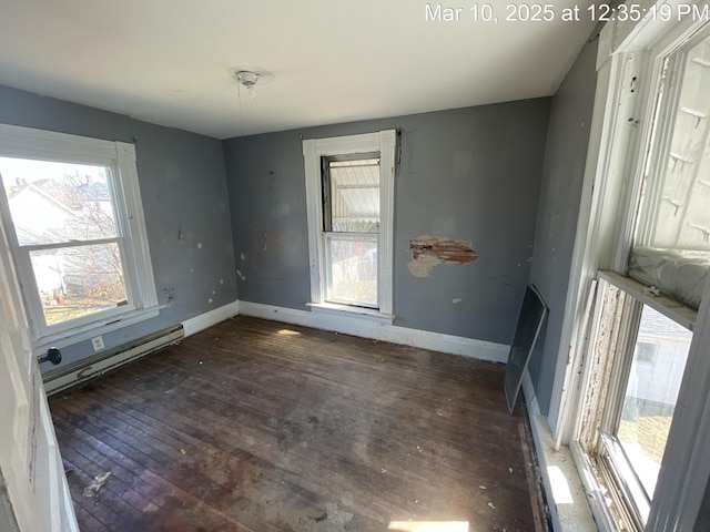 empty room featuring baseboard heating, baseboards, and hardwood / wood-style floors