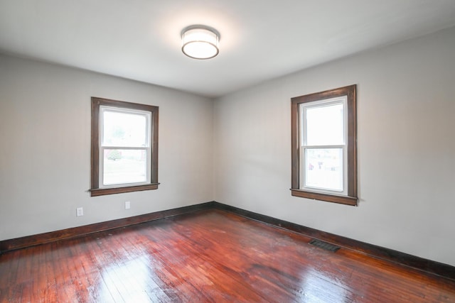 unfurnished room featuring dark wood-type flooring, visible vents, and baseboards