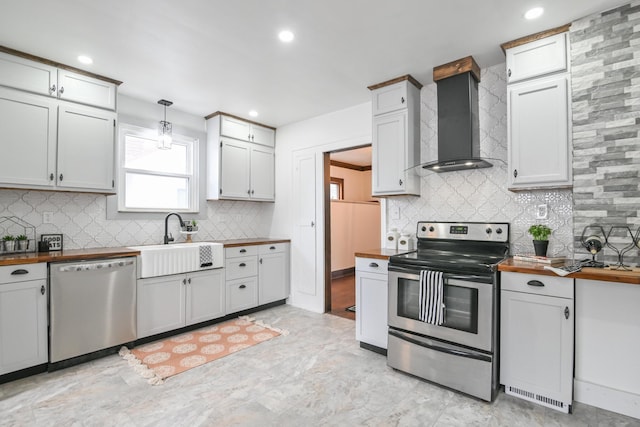 kitchen with wood counters, appliances with stainless steel finishes, decorative light fixtures, wall chimney range hood, and a sink