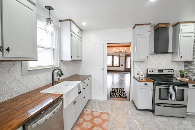 kitchen featuring pendant lighting, stainless steel appliances, butcher block countertops, wall chimney range hood, and an inviting chandelier