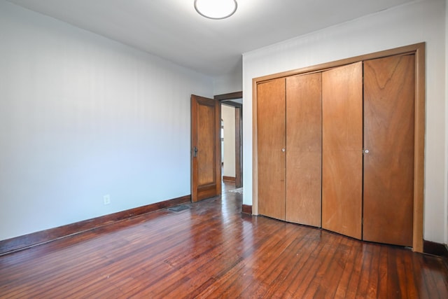 unfurnished bedroom featuring dark wood-type flooring, a closet, and baseboards