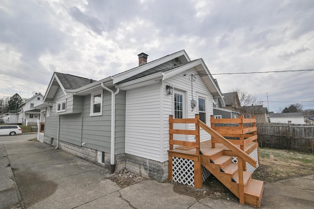 view of property exterior with roof with shingles, fence, and a chimney