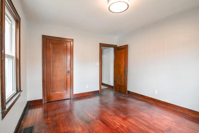 unfurnished bedroom featuring multiple windows, dark wood finished floors, visible vents, and baseboards