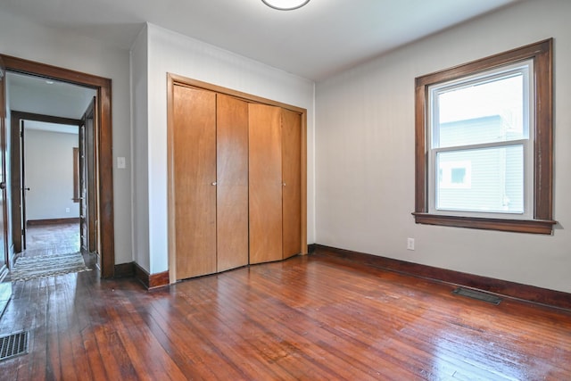 unfurnished bedroom with dark wood-type flooring, a closet, visible vents, and baseboards