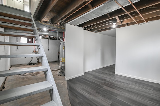 unfinished basement featuring dark wood-style floors, water heater, and baseboards