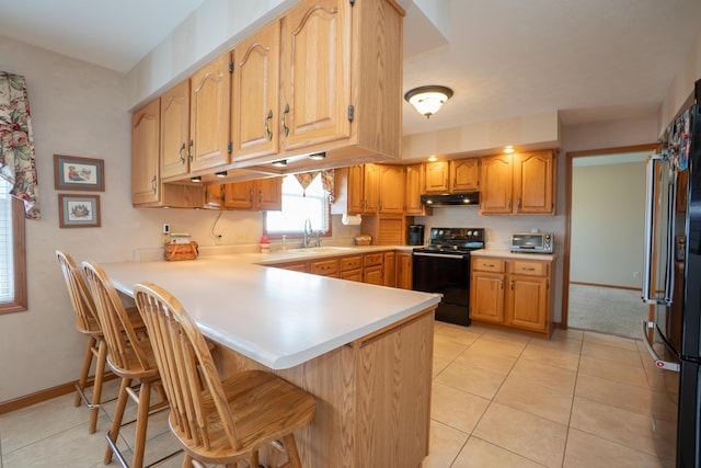kitchen with a peninsula, a breakfast bar, under cabinet range hood, a sink, and black appliances