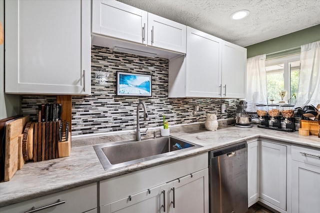 kitchen featuring tasteful backsplash, light countertops, stainless steel dishwasher, white cabinetry, and a sink