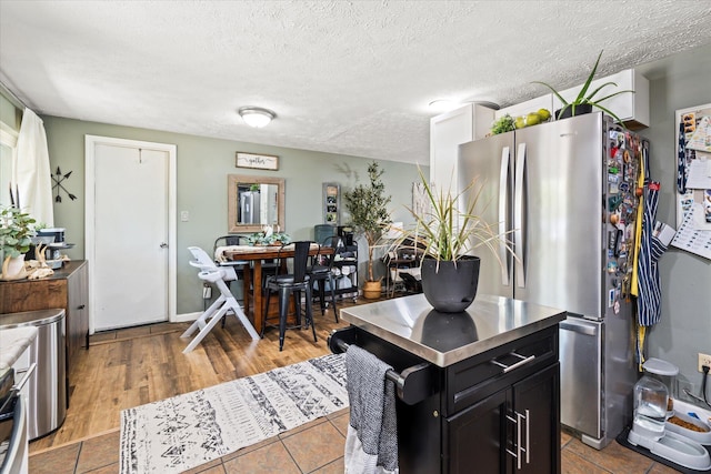 kitchen with stainless steel counters, freestanding refrigerator, a textured ceiling, wood finished floors, and dark cabinetry