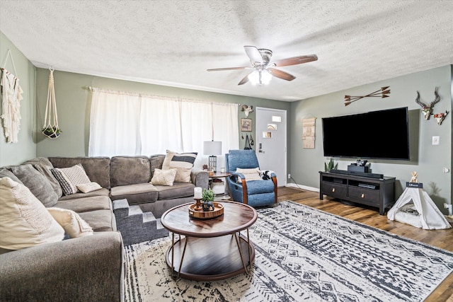 living room featuring a ceiling fan, a textured ceiling, baseboards, and wood finished floors